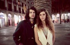 a man and woman standing next to each other in front of a palm tree at night