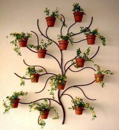 a metal tree with potted plants hanging from it's sides on a wall