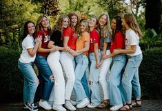 a group of young women standing next to each other in front of trees and bushes