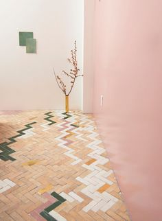 a vase with a small tree in it on a tiled floor next to a pink wall