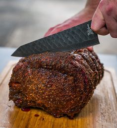 a person holding a knife over a piece of meat on a cutting board