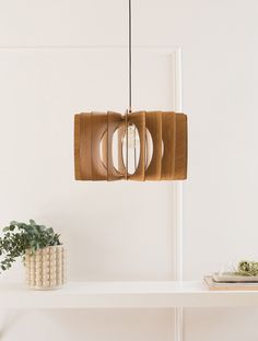 a wooden light fixture hanging over a white shelf next to a vase with flowers on it