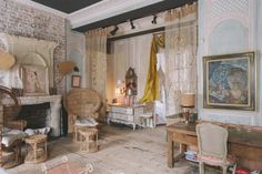 an old fashioned living room with wicker furniture and paintings on the walls, in front of a fireplace