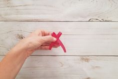 a person is holding a pink ribbon in front of a white wooden wall with planks