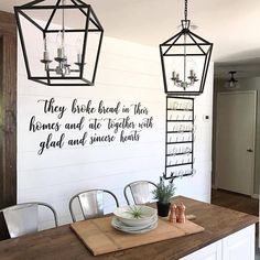 a dining room table with two hanging lights above it and a quote on the wall that says, they broke bread in their bones and ate together with glad and some hearts