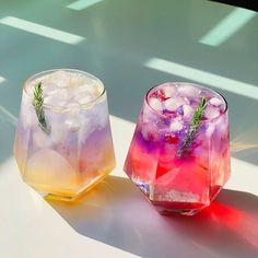 two glasses filled with ice sitting on top of a white table next to each other