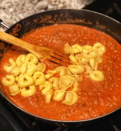 a pan filled with pasta and sauce on top of an oven burner next to a wooden spoon