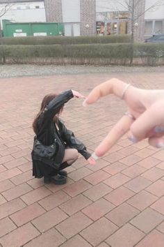 a woman kneeling on the ground with her hand reaching out to someone's finger