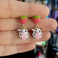 a person is holding two small earrings in their hand, one has a cow and the other has a strawberry on it