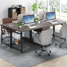 an office desk with two laptops and three monitors on it, in front of a large window