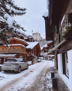 a car parked on the side of a snow covered road in front of wooden buildings