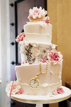 a three tiered white cake with pink flowers and a clock on the bottom layer