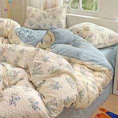 an unmade bed with blue and white comforter on it in front of a window