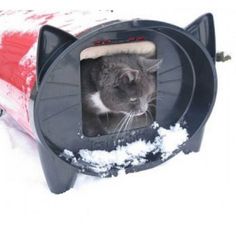 a cat sitting inside of a black and red litter box in the snow with it's eyes closed