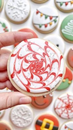 a hand holding a decorated cookie in front of christmas cookies