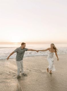 a man and woman holding hands while walking on the beach