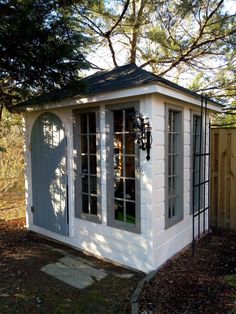 a small white building sitting in the middle of a yard next to a fence and trees