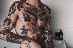 a man with lots of tattoos on his body standing in front of a bathroom sink