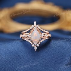 a white opal and diamond ring sitting on top of a blue cloth