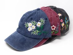 three hats with embroidered flowers on them sitting side by side in front of a white background