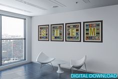 three framed pictures hang on the wall next to chairs in an empty room with large windows