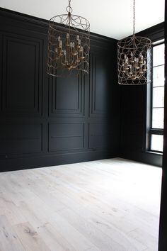 an empty room with two chandeliers hanging from it's ceiling and black walls