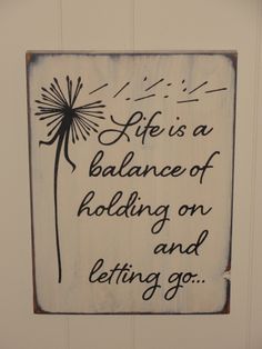 a wooden sign that says life is a balance of holding on and letting go with dandelions