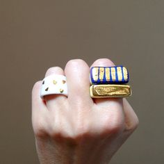 a woman's hand holding two rings with gold and blue designs on them,