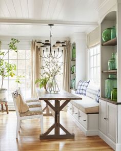 a dining room table and chairs in front of a window with potted plants on it