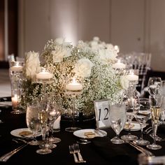 the table is set with white flowers, candles and silverware for an elegant wedding reception