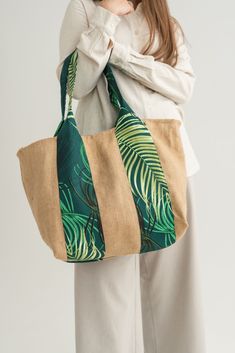 a woman is holding a large bag with palm leaves on the front and bottom panels