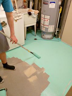 a man using a paint roller on the floor in front of a water heater