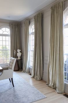 an elegant dining room with large windows and beige drapes on the window sill