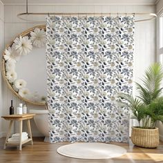 a bathroom with a flower shower curtain next to a round mirror and potted plant