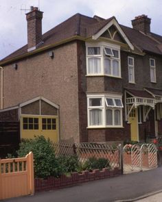 a large brown house with white trim on the front and side windows, next to a fence