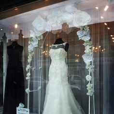 a wedding dress is on display in a store window with flowers and ribbons around it