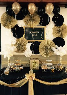 black and gold dessert table with candy bar sign, paper fan decorations, and tissue pom poms