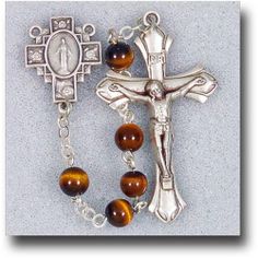 Adorned with brown and gold semi precious stones, the 6 mm Genuine Gem Stone Tiger Eye Rosary makes a fierce statement in religious accessories. Matching silver tone accents bring out the various hues of each bead, creating a lovely article of the faith to be placed in an equally dainty giftbox. Spiritual Nickel-free Brown Jewelry, Brown Crucifix Spiritual Jewelry, Brown Spiritual Crucifix Jewelry, Spiritual Brown Crucifix Jewelry, Brown Crucifix Jewelry Gift, Brown Crucifix Jewelry For Gifts, Brown Beaded Spiritual Rosary, Communion Sets, Rosary Boxes