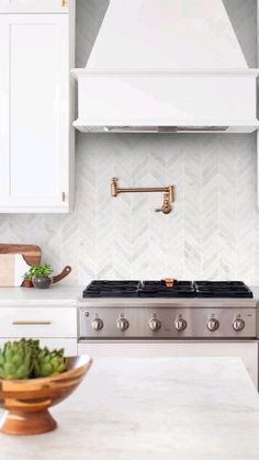 a kitchen with white cabinets and stainless steel range hood over the stove, surrounded by potted succulents