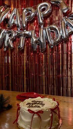 a birthday cake sitting on top of a wooden table next to balloons that say happy birthday