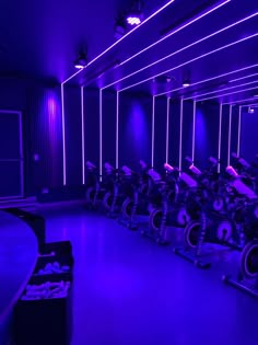 there are many exercise bikes in this room with purple lighting on the walls and floor