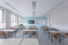 an empty classroom with desks, chairs and a flat screen tv on the wall