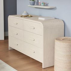 a white dresser sitting on top of a hard wood floor next to a shelf filled with vases