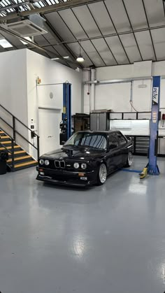 a black car parked in a garage next to stairs and railings on the floor