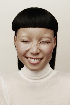 a woman with black hair smiling and wearing a white turtle neck sweater over her shoulders