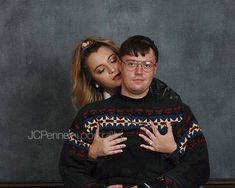 a man and woman hugging each other in front of a wall