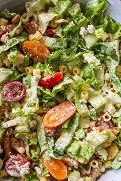 a salad in a bowl with tomatoes, pasta and other toppings on the side