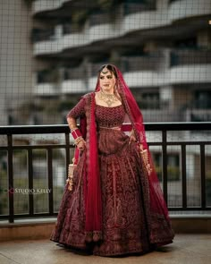 a woman in a red and gold bridal gown standing on a balcony with her hands on her hips