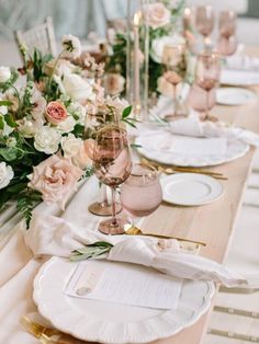 the table is set with white and gold plates, silverware, and pink flowers