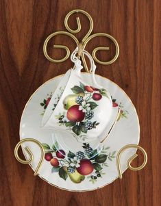 a tea set with fruit on it is hanging from a wooden wall, and sits on a saucer